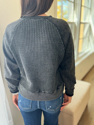 Person wearing a textured gray sweater and blue jeans in a room with a window.