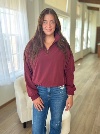 Woman wearing a maroon long-sleeve shirt and blue jeans indoors.
