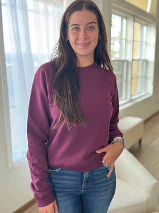 Woman wearing a purple sweatshirt and blue jeans indoors.