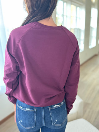 Person wearing a purple sweatshirt and blue jeans in a room with large windows.