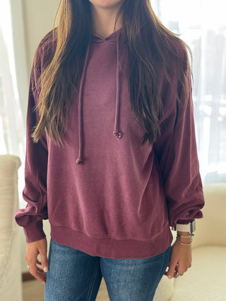 Person wearing a maroon hoodie and blue jeans indoors.