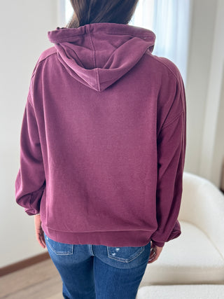 Person wearing a purple hoodie and blue jeans in a room with white walls and a white chair.