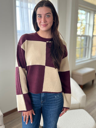 Woman wearing a checkered sweater in a room with large windows.