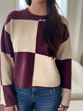 Person wearing a checkered sweater with maroon and beige colors.