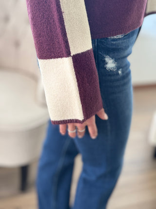 Person wearing a purple and white checkered scarf with blue jeans indoors.