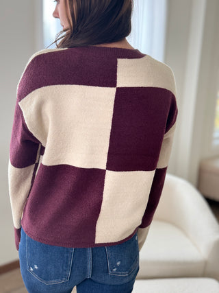 Person wearing a checkered sweater with purple and beige pattern indoors.