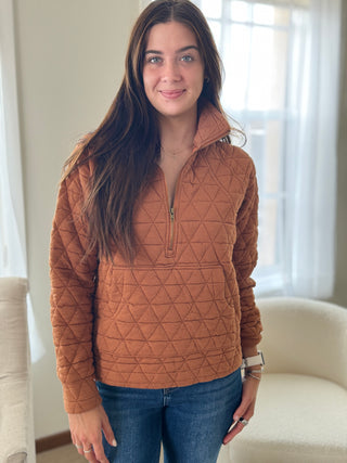 Woman wearing a brown quilted pullover in a room with light-colored walls and furniture.