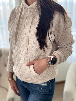 Person wearing a beige quilted jacket with a blurred indoor background