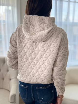 Person wearing a beige quilted jacket in a room with light-colored walls.