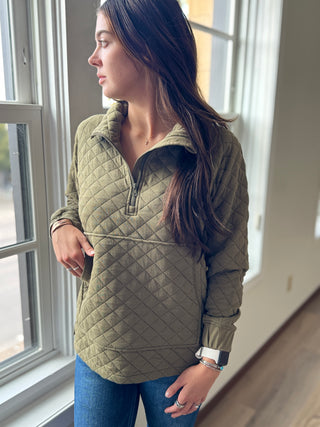 Woman wearing a green quilted jacket standing by a window