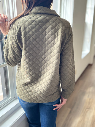 Person wearing a quilted green jacket standing by a window