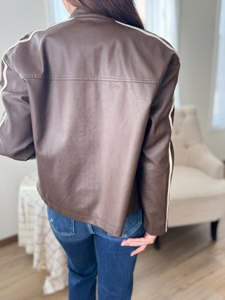 Person wearing a brown leather jacket with white stripes on a neutral background