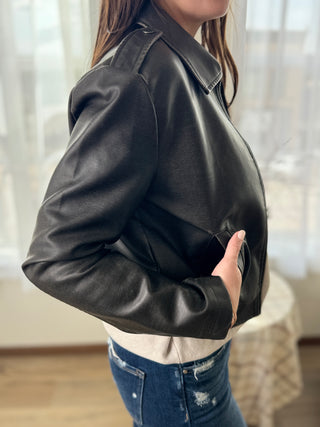 Person wearing a black leather jacket indoors with a blurred background