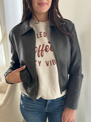 Person wearing a black leather jacket over a graphic t-shirt with text.