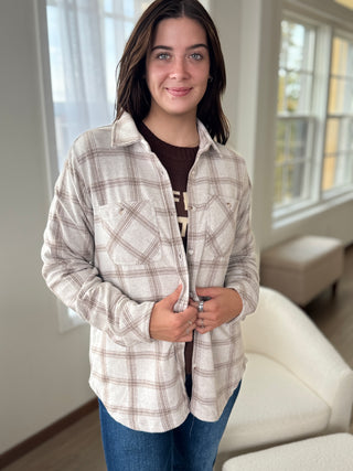Woman wearing a plaid shirt in a room with large windows.