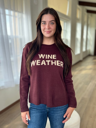 Woman wearing a maroon sweater with 'WINE WEATHER' text indoors.