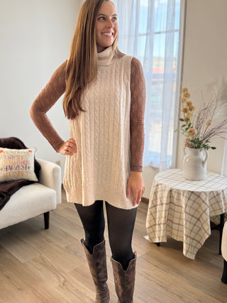 Woman wearing a beige tunic and brown knee-high boots in a living room.