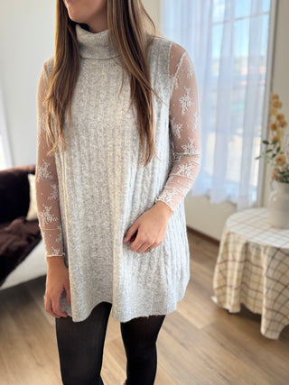 Person wearing a long, light gray sweater with lace details in a bright room.
