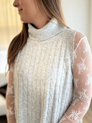 Woman wearing a light gray sweater with sheer sleeves featuring floral patterns.