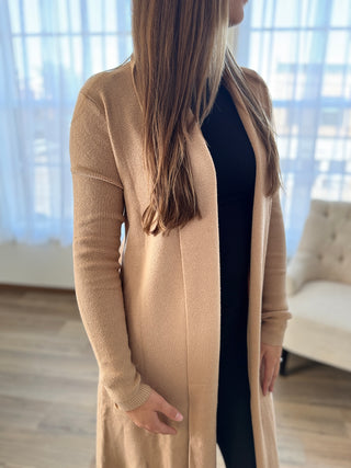 Person wearing a long beige cardigan in a room with light-colored furniture.