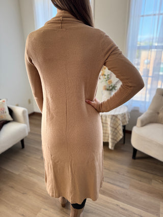 Person wearing a beige long-sleeve dress in a room with furniture and decor.