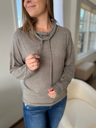 Woman wearing a gray hoodie and blue jeans indoors.