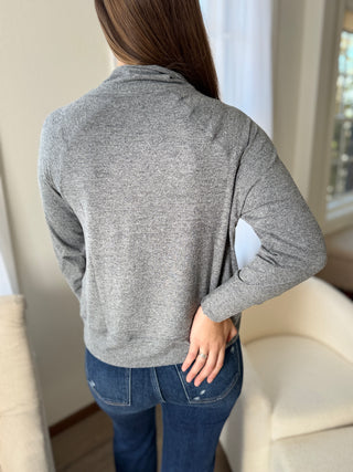 Person wearing a gray long-sleeve top with elbow patches in a neutral indoor setting