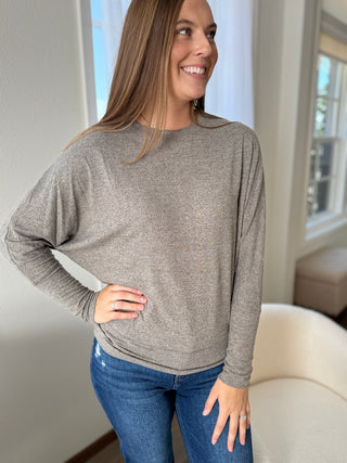 Woman wearing a gray sweater and blue jeans indoors.
