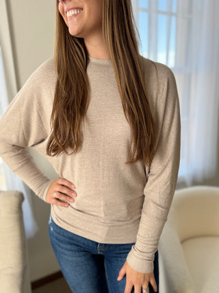 Woman wearing a beige sweater and blue jeans indoors.