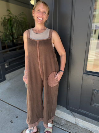 Woman wearing a brown sleeveless dress with a pocket standing outside a building.