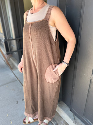 Person wearing a brown checkered dress standing against a dark wall.