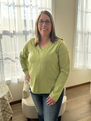 Woman wearing a green sweater standing in a room with curtains and furniture.