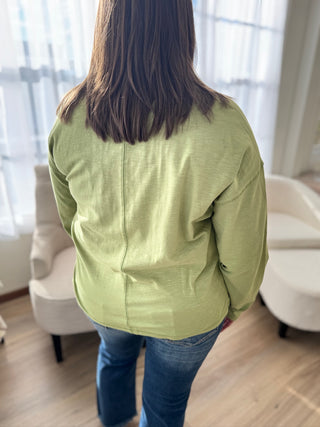 Person wearing a green jacket in a room with light-colored curtains and furniture.