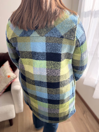 Person wearing a blue and green plaid shirt in a room with a couch and window.