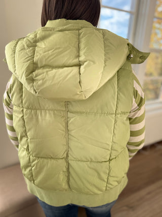 Person wearing a light green puffer vest indoors with a window in the background