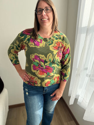 Woman wearing a colorful floral sweater and jeans indoors.