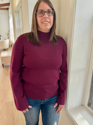 Person wearing a maroon sweater and blue jeans indoors.