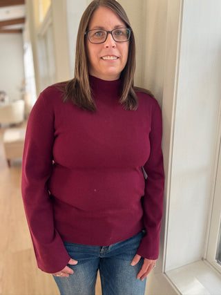 Person wearing a maroon sweater and blue jeans indoors.