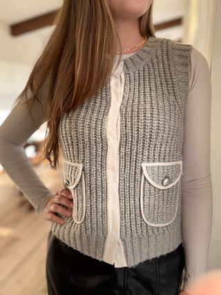 Person wearing a gray knitted vest with white trim