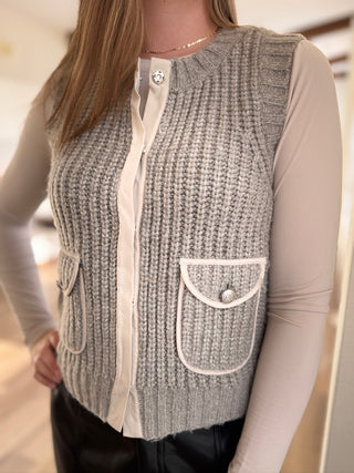 Gray knitted vest with white trim worn by a person indoors