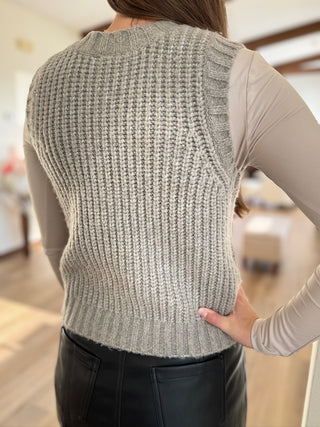 Person wearing a gray knitted vest indoors