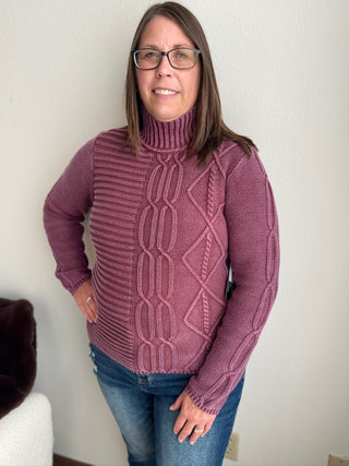 Person wearing a purple cable knit sweater against a plain background