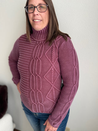 Woman wearing a purple cable knit sweater against a plain background