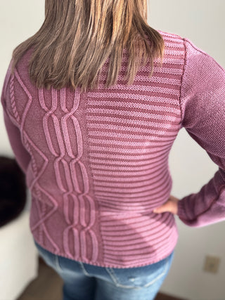 Person wearing a pink sweater with a geometric pattern, standing against a neutral background.