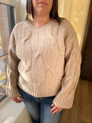 Person wearing a beige cable knit sweater indoors.