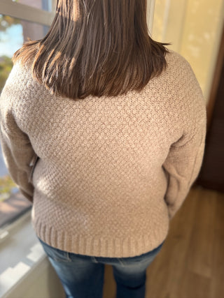 Person wearing a beige sweater standing by a window