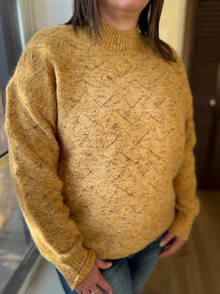 Person wearing a mustard yellow sweater with a textured pattern indoors.