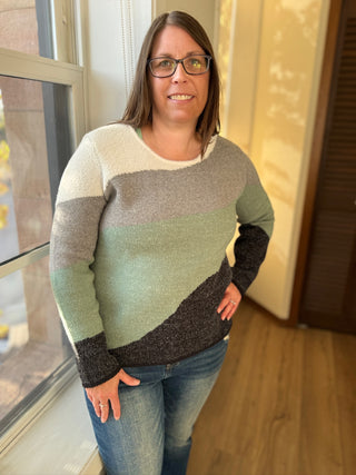 Woman wearing a colorful sweater standing indoors near a window.