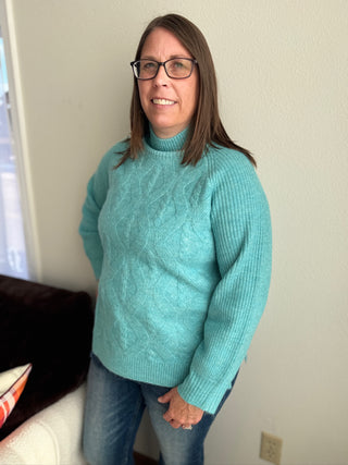Person wearing a teal sweater standing against a neutral wall.
