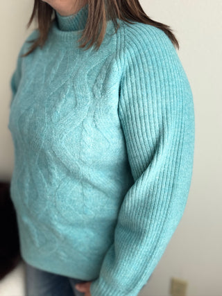 Teal sweater worn by a person against a neutral background